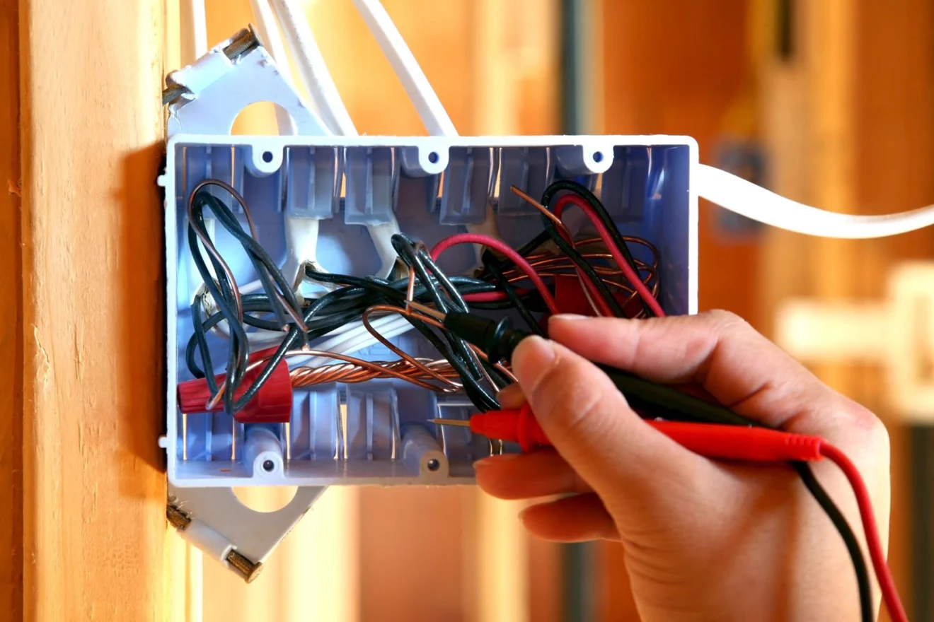 Electrician testing wiring in a wall box with a multimeter
